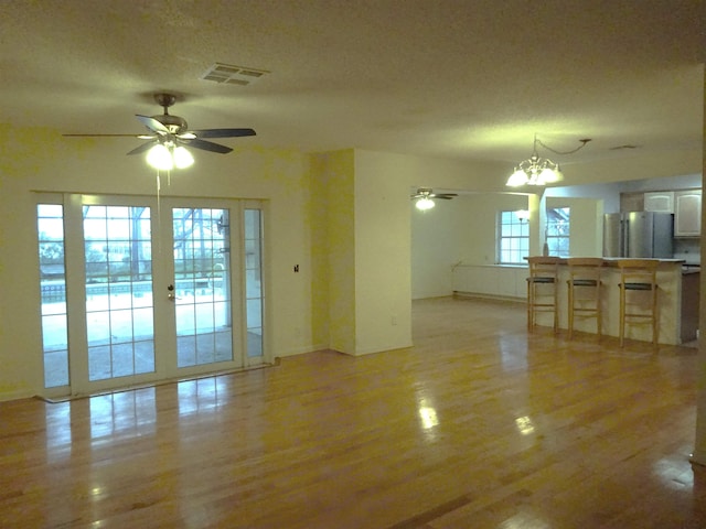 unfurnished living room featuring ceiling fan with notable chandelier, light wood finished floors, a textured ceiling, and visible vents