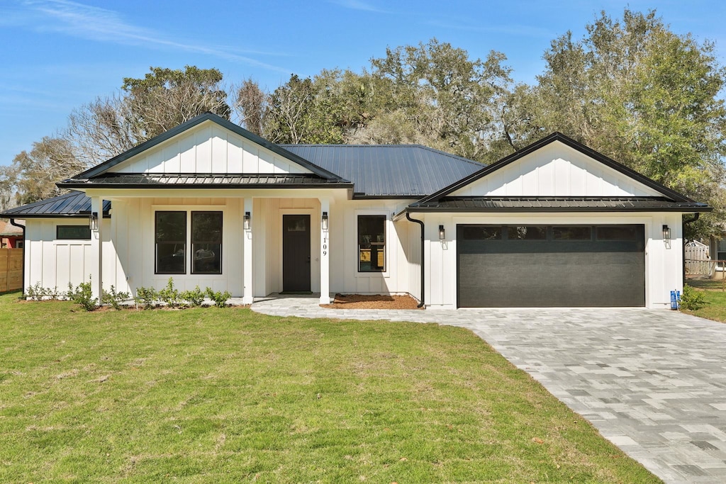 modern farmhouse style home featuring decorative driveway, an attached garage, board and batten siding, a front yard, and metal roof