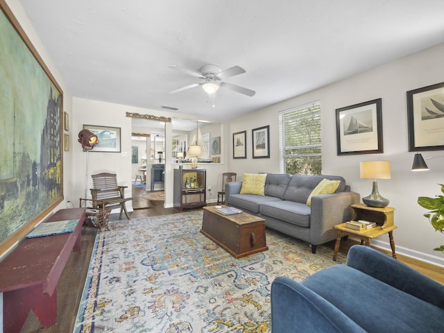living room with baseboards, wood finished floors, visible vents, and a ceiling fan