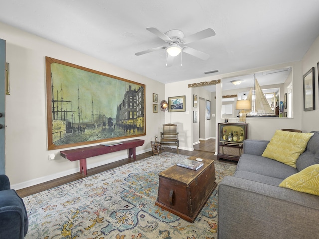 living room featuring a ceiling fan, wood finished floors, visible vents, and baseboards