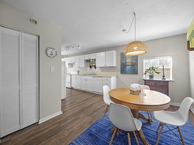 dining room with track lighting, dark wood finished floors, and baseboards