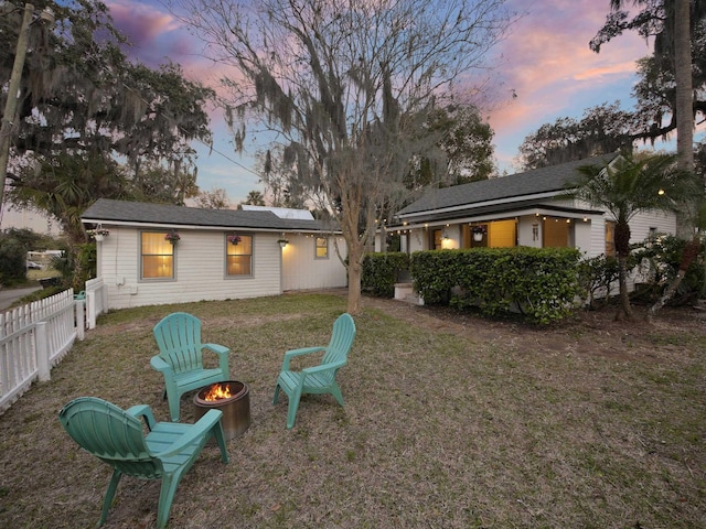 back of property at dusk featuring a yard, an outdoor fire pit, fence, and roof mounted solar panels