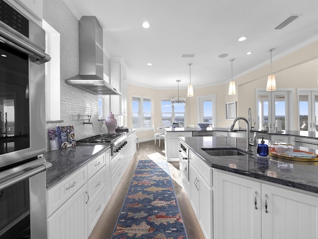 kitchen featuring white cabinets, wall chimney exhaust hood, sink, and appliances with stainless steel finishes