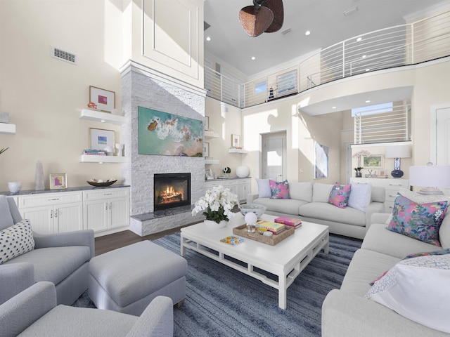 living room featuring a stone fireplace, ceiling fan, a towering ceiling, and dark wood-type flooring