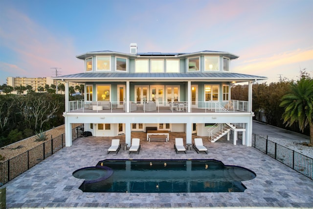 back house at dusk with a patio, a pool with hot tub, and solar panels