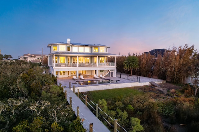 back house at dusk with solar panels, an outdoor hangout area, a balcony, a pool, and a patio