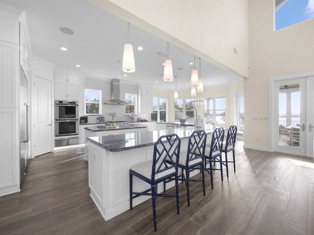 kitchen with white cabinets, dark wood-type flooring, a large island, and wall chimney range hood