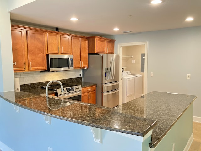 kitchen with a breakfast bar area, dark stone countertops, kitchen peninsula, stainless steel appliances, and washing machine and clothes dryer