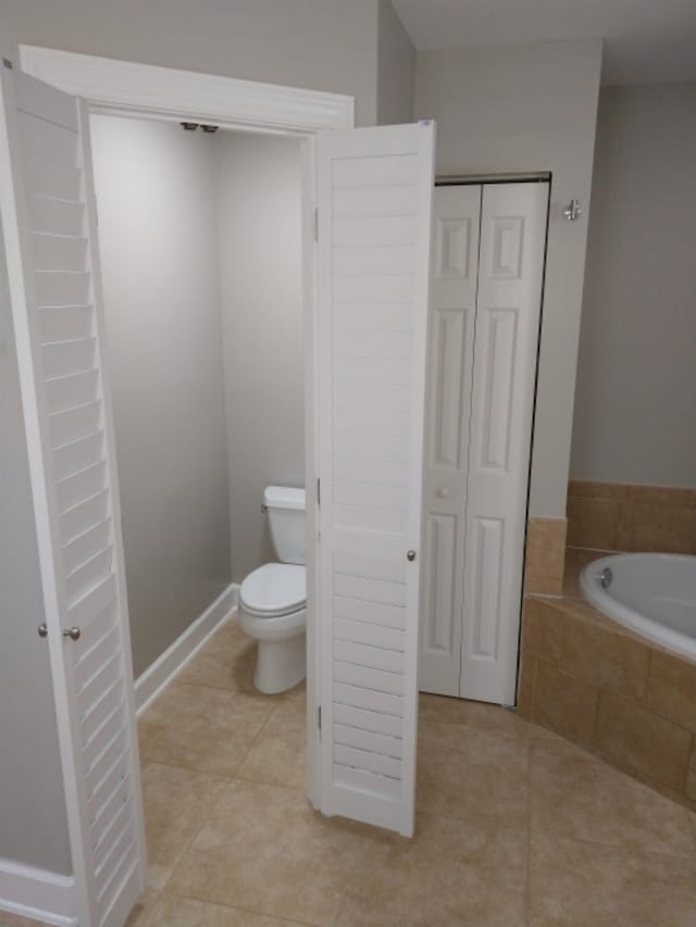 bathroom with tile patterned flooring, tiled bath, and toilet