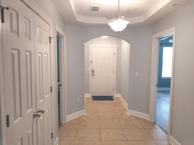 hall featuring light tile patterned floors and a tray ceiling