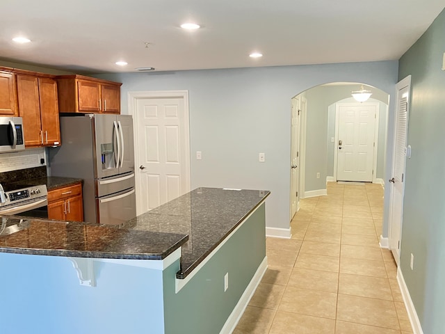 kitchen with dark stone counters, a breakfast bar, light tile patterned floors, and stainless steel appliances