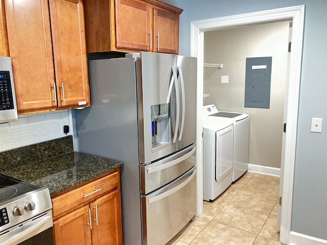 kitchen with appliances with stainless steel finishes, dark stone counters, light tile patterned floors, washing machine and clothes dryer, and electric panel