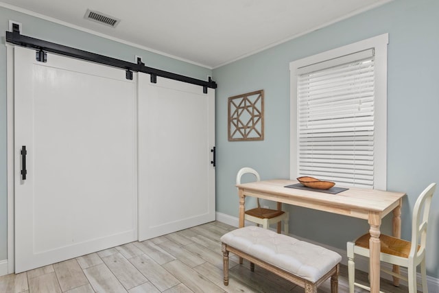 dining space with a barn door, light hardwood / wood-style flooring, and ornamental molding