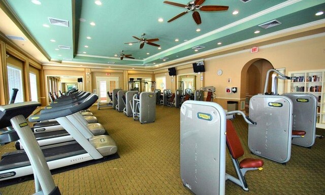 exercise room featuring carpet, a raised ceiling, and ornamental molding