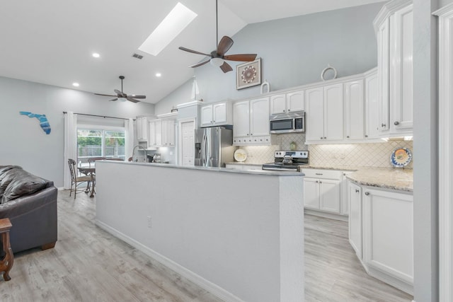 kitchen featuring appliances with stainless steel finishes, a skylight, high vaulted ceiling, light hardwood / wood-style flooring, and white cabinets