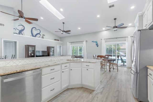 kitchen with appliances with stainless steel finishes, a skylight, white cabinetry, and light stone counters