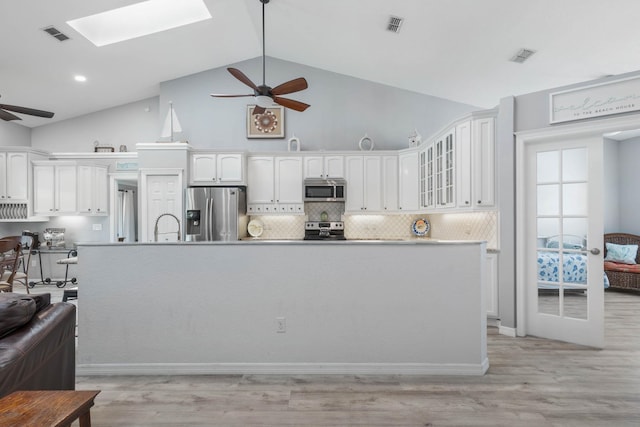 kitchen with backsplash, white cabinets, a skylight, light wood-type flooring, and stainless steel appliances