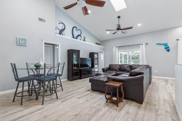 living room with ceiling fan, light hardwood / wood-style floors, high vaulted ceiling, and a skylight