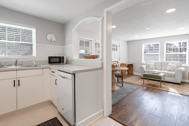 kitchen featuring a wealth of natural light, white cabinetry, dishwasher, sink, and light hardwood / wood-style flooring