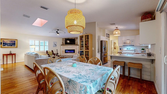 dining area with a skylight, ceiling fan, sink, hardwood / wood-style floors, and a stone fireplace