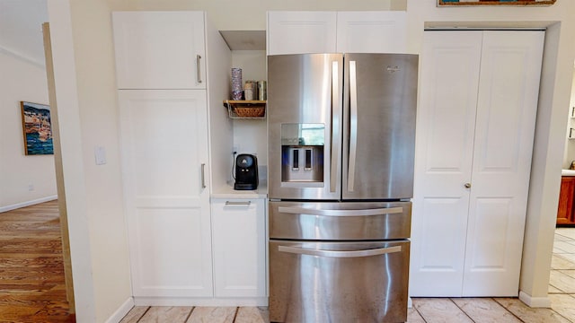 kitchen featuring stainless steel fridge, white cabinetry, and light tile patterned floors