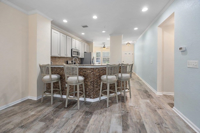 kitchen featuring appliances with stainless steel finishes, a breakfast bar, crown molding, and light wood finished floors