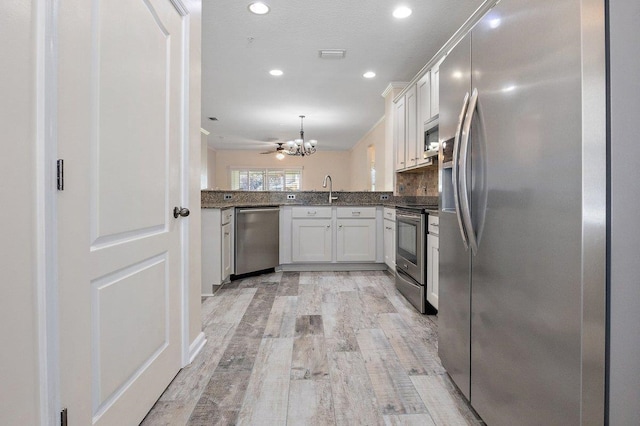 kitchen with stainless steel appliances, decorative light fixtures, light wood-style flooring, and white cabinets