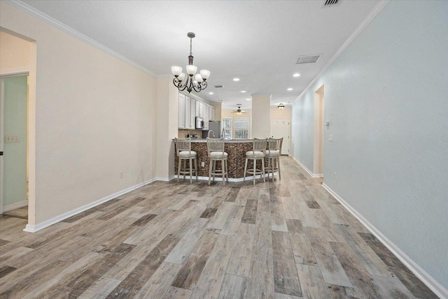 unfurnished dining area with ornamental molding, visible vents, light wood-style floors, and baseboards