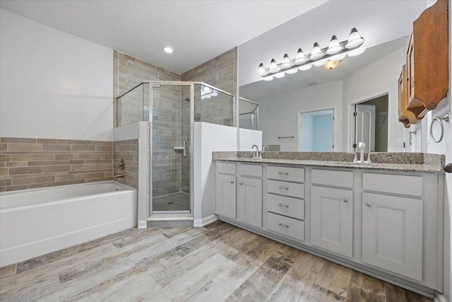 bathroom featuring a textured ceiling, wood finished floors, a shower stall, a bath, and double vanity