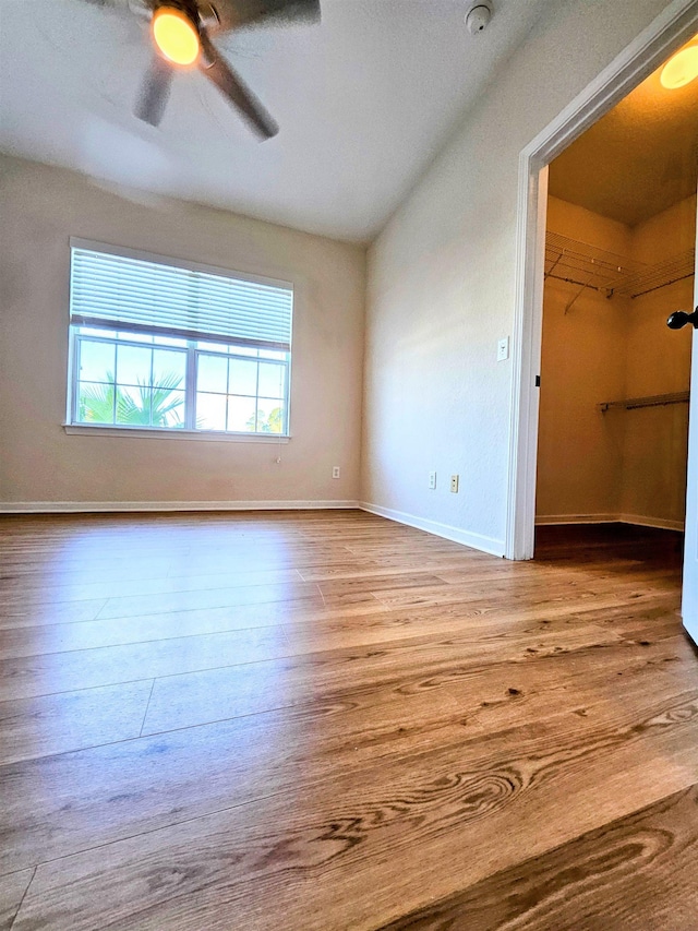 unfurnished bedroom featuring baseboards, a ceiling fan, wood finished floors, and a walk in closet