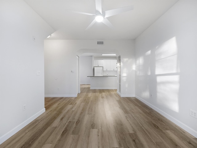 unfurnished living room with baseboards, a ceiling fan, arched walkways, and light wood-style floors