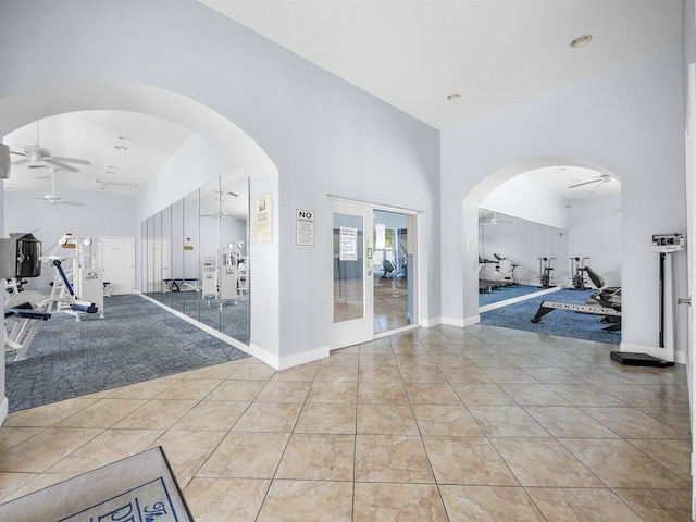 exercise room featuring ceiling fan, light tile patterned floors, a towering ceiling, and french doors