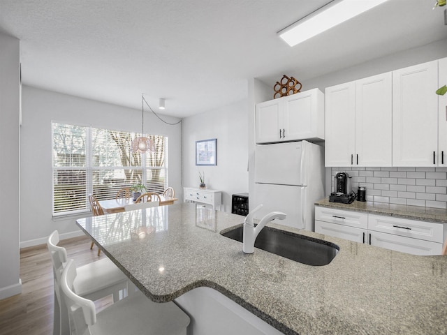 kitchen with white cabinetry, a sink, freestanding refrigerator, and backsplash