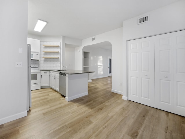 kitchen featuring visible vents, arched walkways, a sink, white appliances, and a peninsula