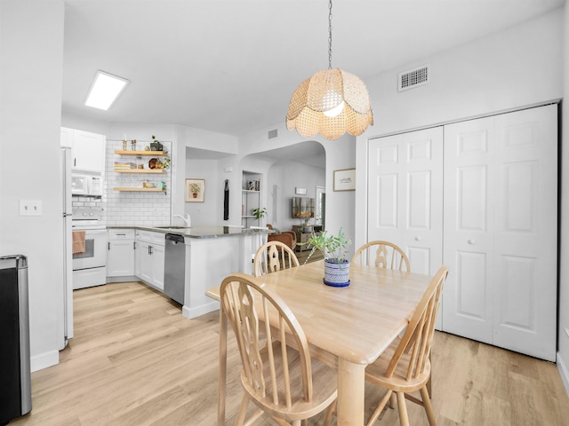 dining area featuring light wood-type flooring, a notable chandelier, visible vents, and arched walkways
