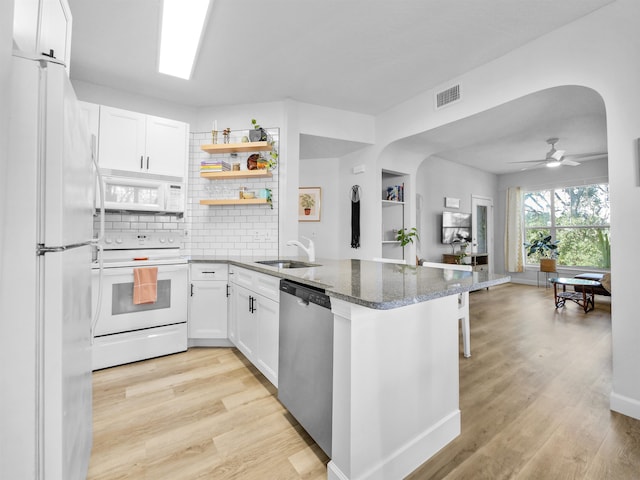 kitchen with white appliances, a peninsula, visible vents, arched walkways, and a sink