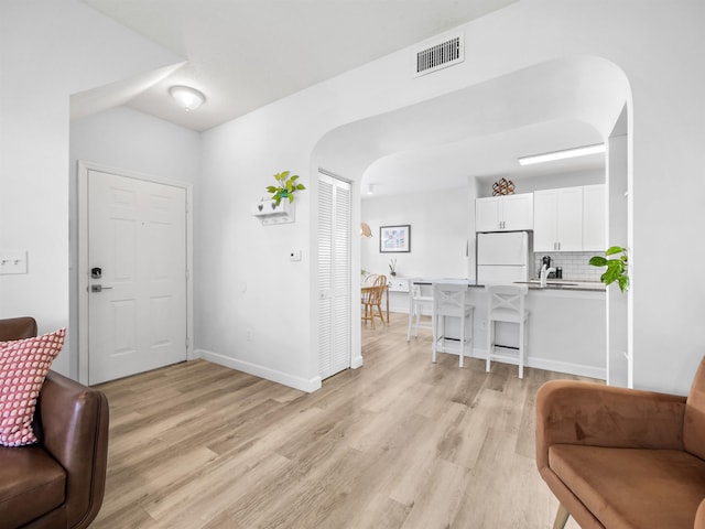 foyer entrance with light wood-style floors, arched walkways, visible vents, and baseboards