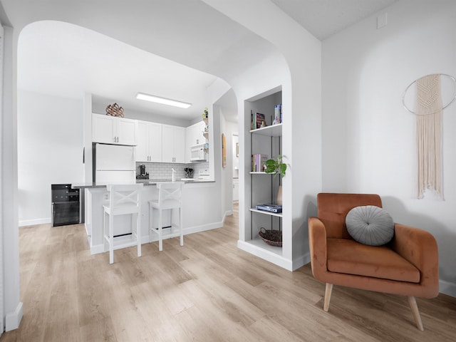 kitchen featuring kitchen peninsula, white appliances, a kitchen bar, white cabinets, and light wood-type flooring