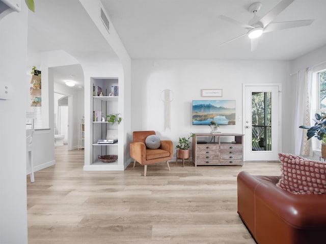 sitting room featuring arched walkways, light wood-style floors, visible vents, and a ceiling fan