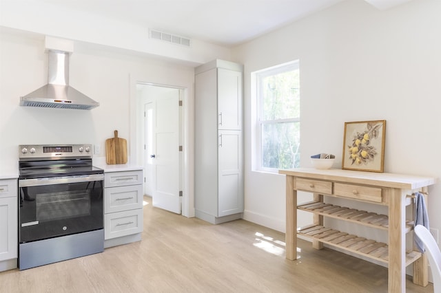 974 Alexander St, Saint Augustine, FL 32084 - kitchen featuring stainless steel electric range oven, wall chimney range hood, light wood-style flooring, light countertops, and white cabinetry