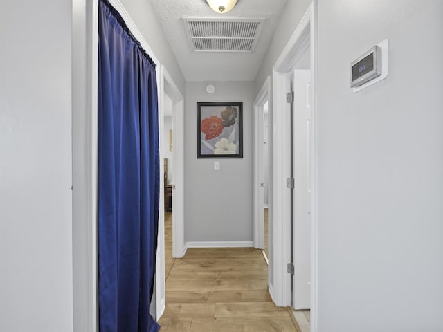 hall with a textured ceiling and light wood-type flooring