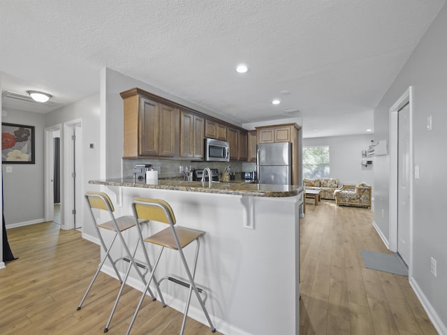 kitchen with a textured ceiling, light wood-type flooring, kitchen peninsula, and stainless steel appliances