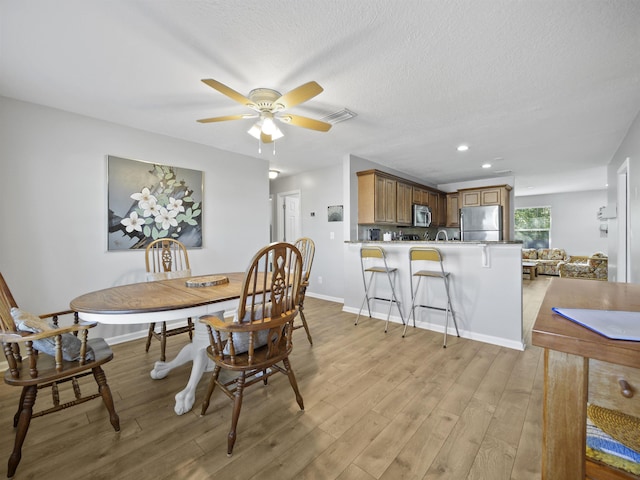 dining space with a textured ceiling, light wood-type flooring, and ceiling fan