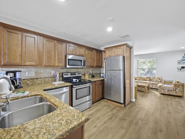 kitchen with sink, tasteful backsplash, light stone counters, light hardwood / wood-style floors, and appliances with stainless steel finishes