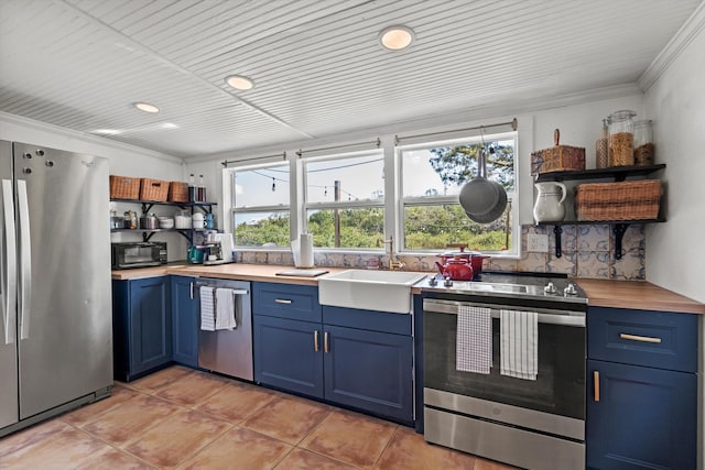 29 Oak St, Saint Augustine, FL 32084 - kitchen with appliances with stainless steel finishes, blue cabinets, open shelves, light tile patterned floors, and butcher block counters