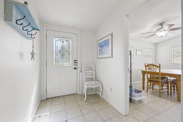 doorway to outside featuring light tile patterned floors, a ceiling fan, and baseboards