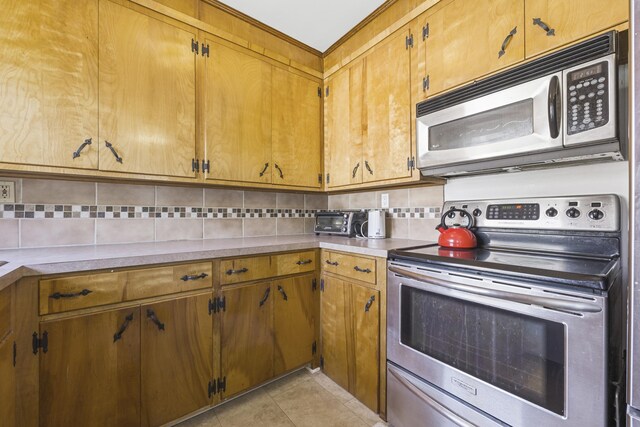 kitchen with tasteful backsplash, stainless steel appliances, light tile patterned flooring, brown cabinetry, and light countertops