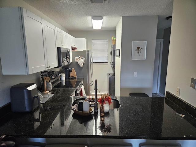 650 W Pope Rd Unit 279, Saint Augustine, FL 32080 - kitchen with appliances with stainless steel finishes, stacked washer / drying machine, dark stone counters, a textured ceiling, and white cabinets
