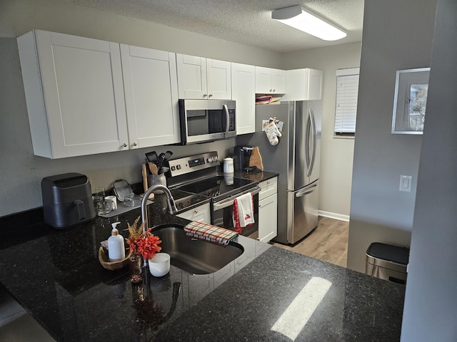 kitchen with white cabinetry, sink, dark stone countertops, a textured ceiling, and appliances with stainless steel finishes