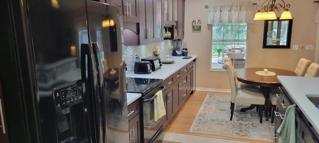 kitchen featuring a notable chandelier, backsplash, light hardwood / wood-style floors, pendant lighting, and black appliances